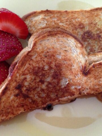 grilled peanut butter and jelly sandwich cut in half on yellow plate with strawberries