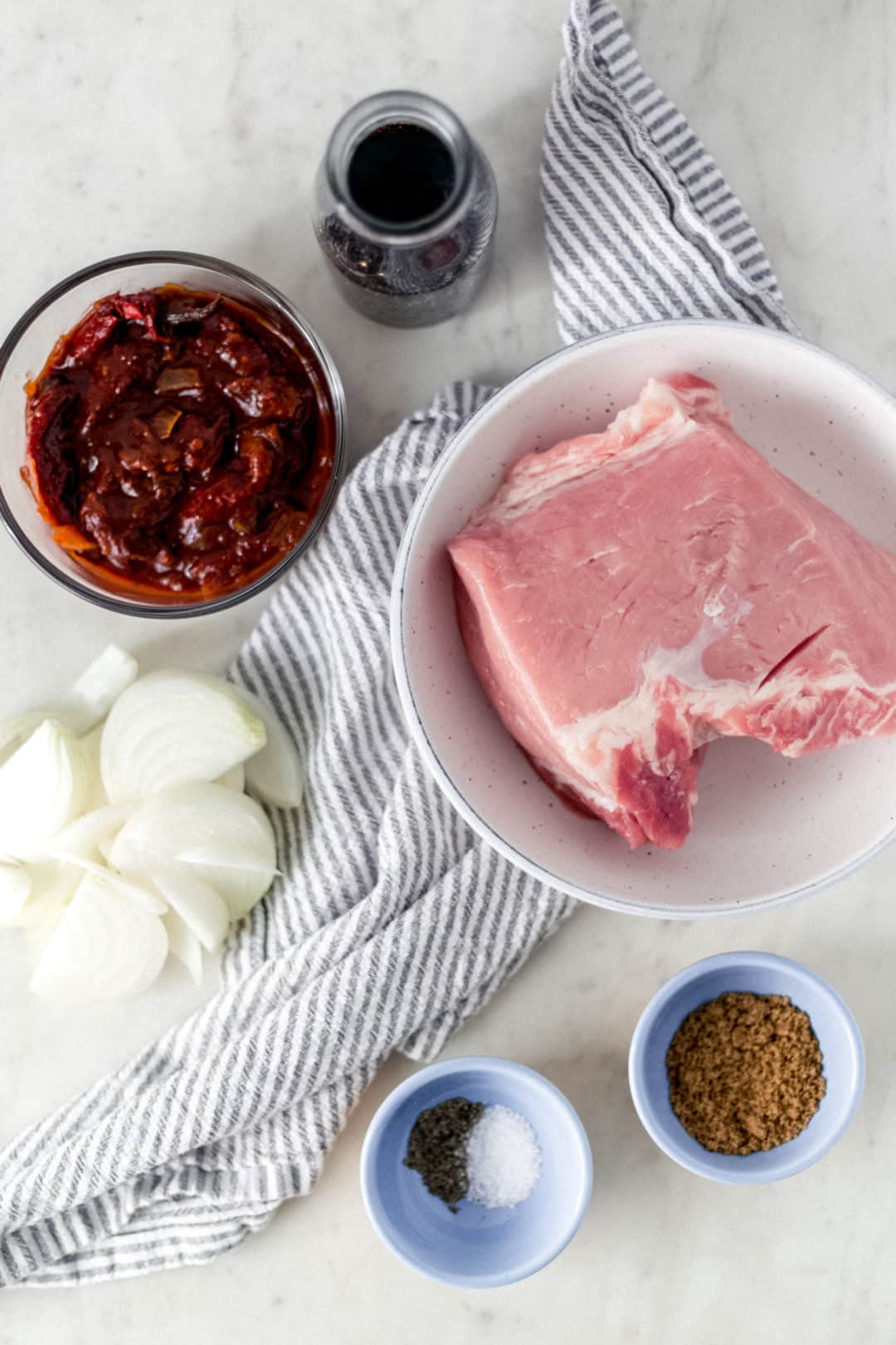 ingredients needed to make pulled pork in separate bowls and containers with a cloth napkin
