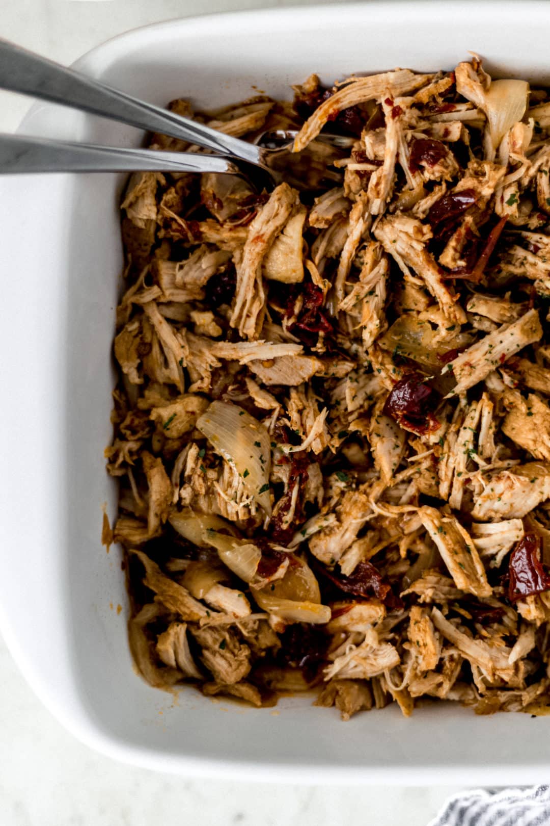 close up view of pulled pork in white baking dish with forks 