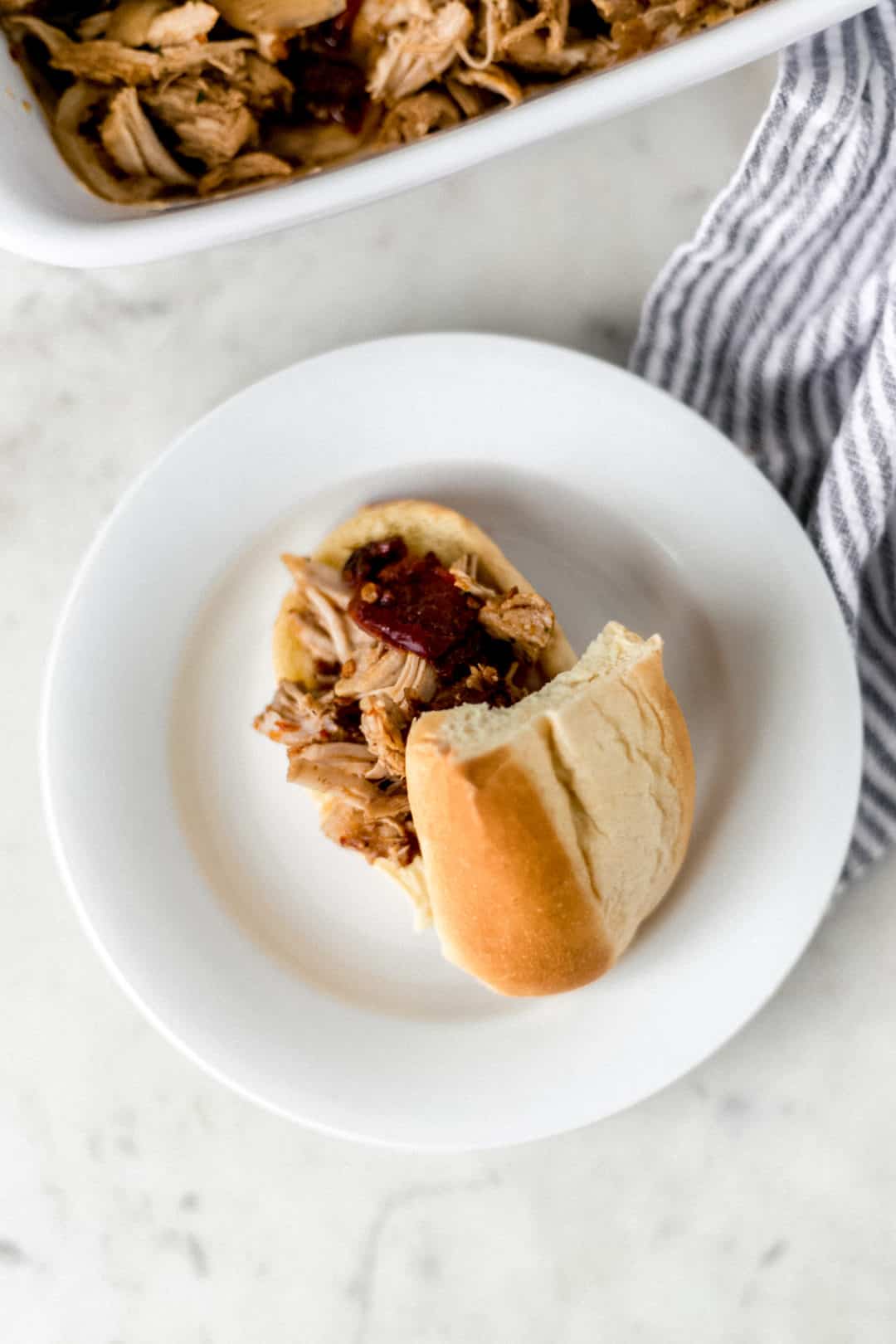 bun with pulled pork on it on a white plate beside a cloth napkin 