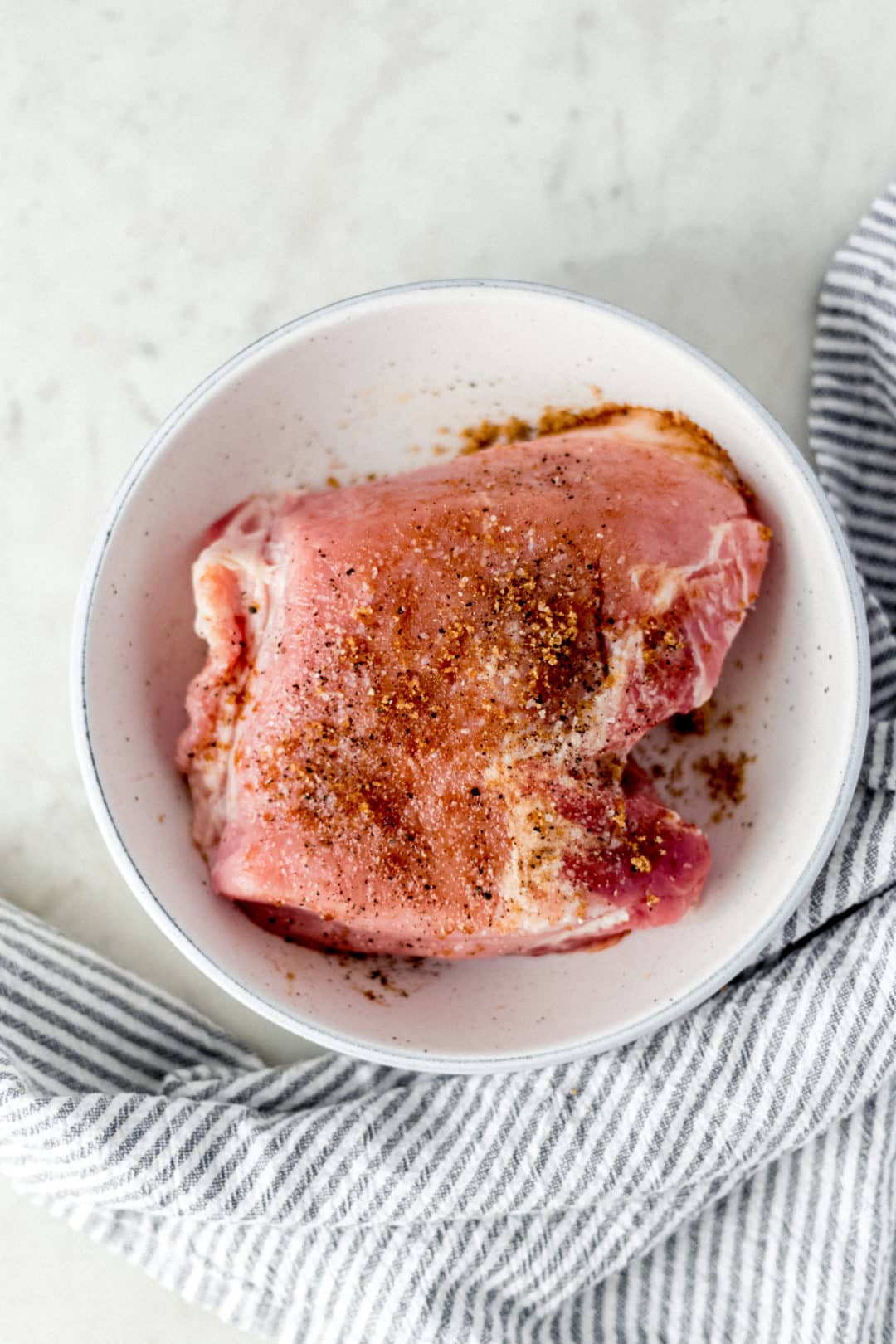 seasoned raw pork in large white bowl beside cloth napkin 