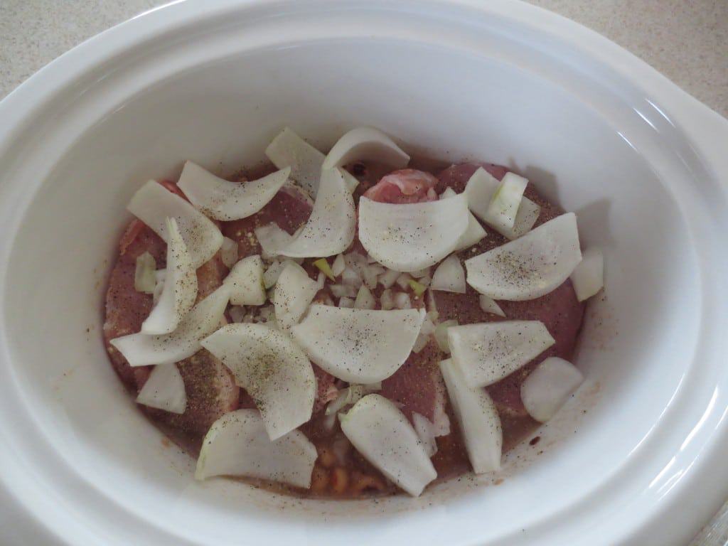 pork chops topped with chopped onion in slow cooker 