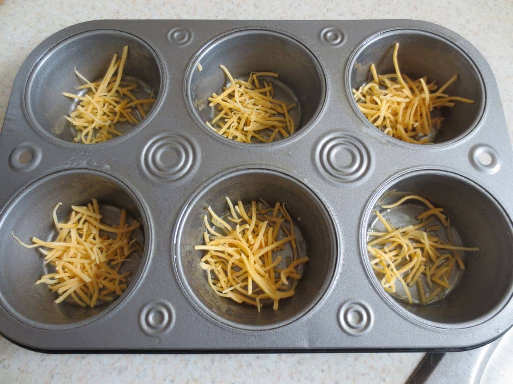 shredded cheese place in the bottom of a muffin pan 
