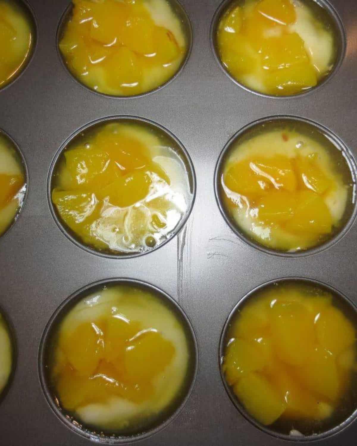 Cobbler mixture and peaches added to muffin pan. 