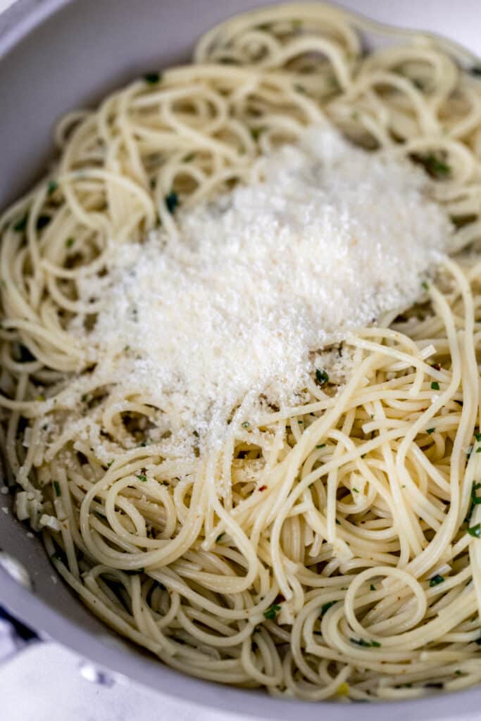 grated parmesan cheese added to cooked spaghetti in skillet 