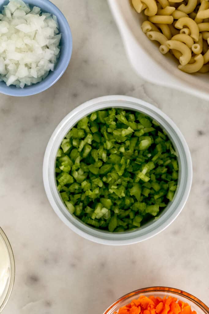 ingredients for warm macaroni salad in small bowls with shopped celery in the center 