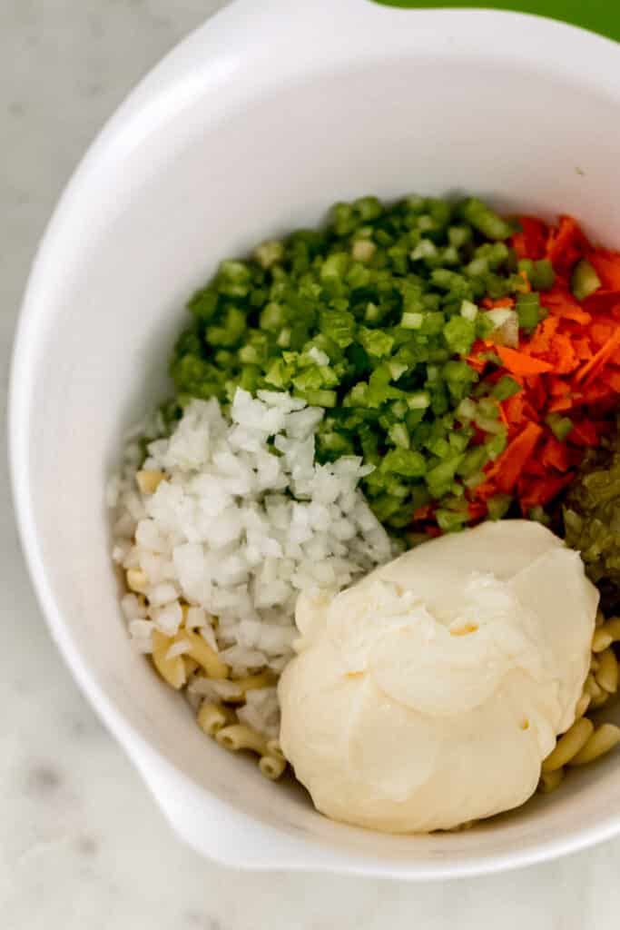 ingredients for macaroni salad all together in a large white mixing bowl 