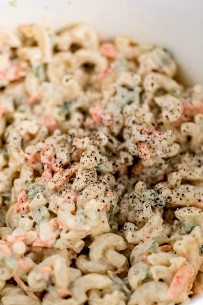 warm macaroni salad in large white mixing bowl topped with salt and ground black pepper 