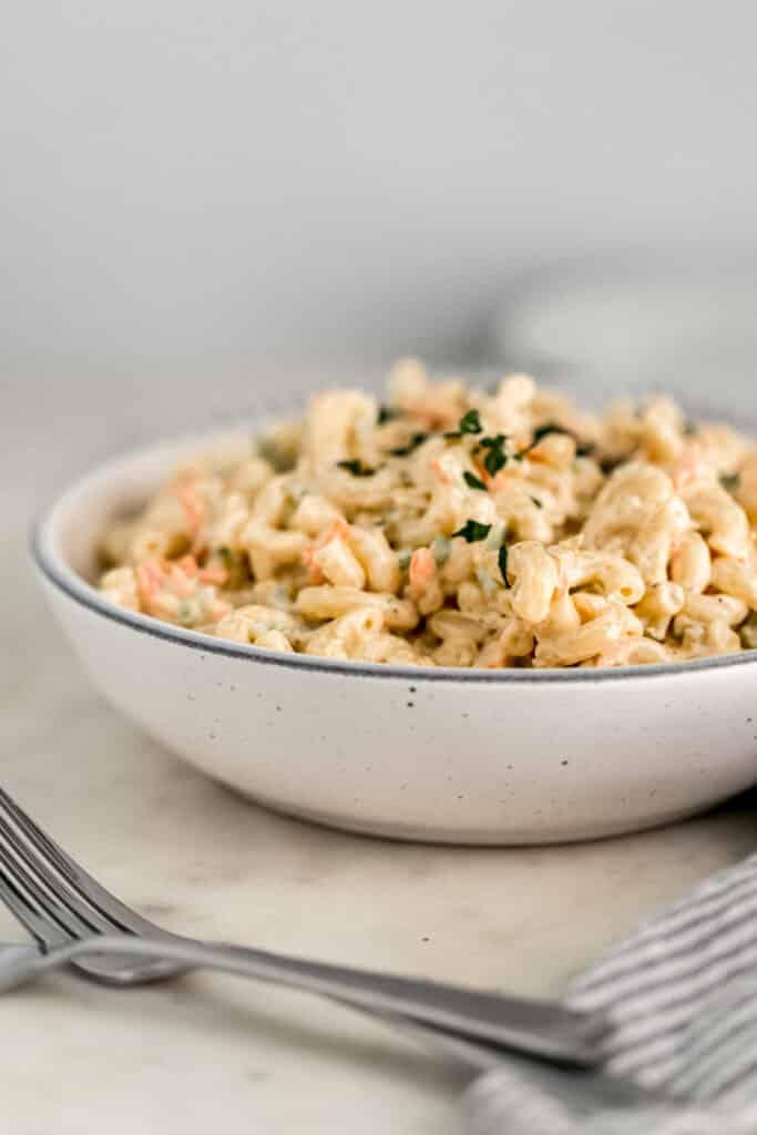 close up side view warm macaroni salad in large white serving bowl with fork and cloth napkin 
