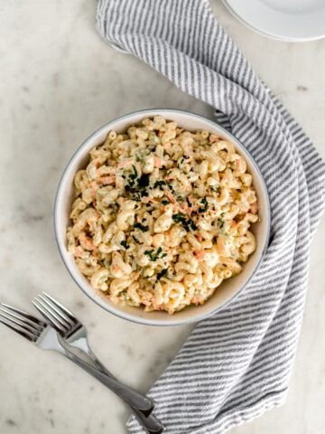 overhead view macaroni salad in a large white bowl with forks, white plates, and cloth napkin