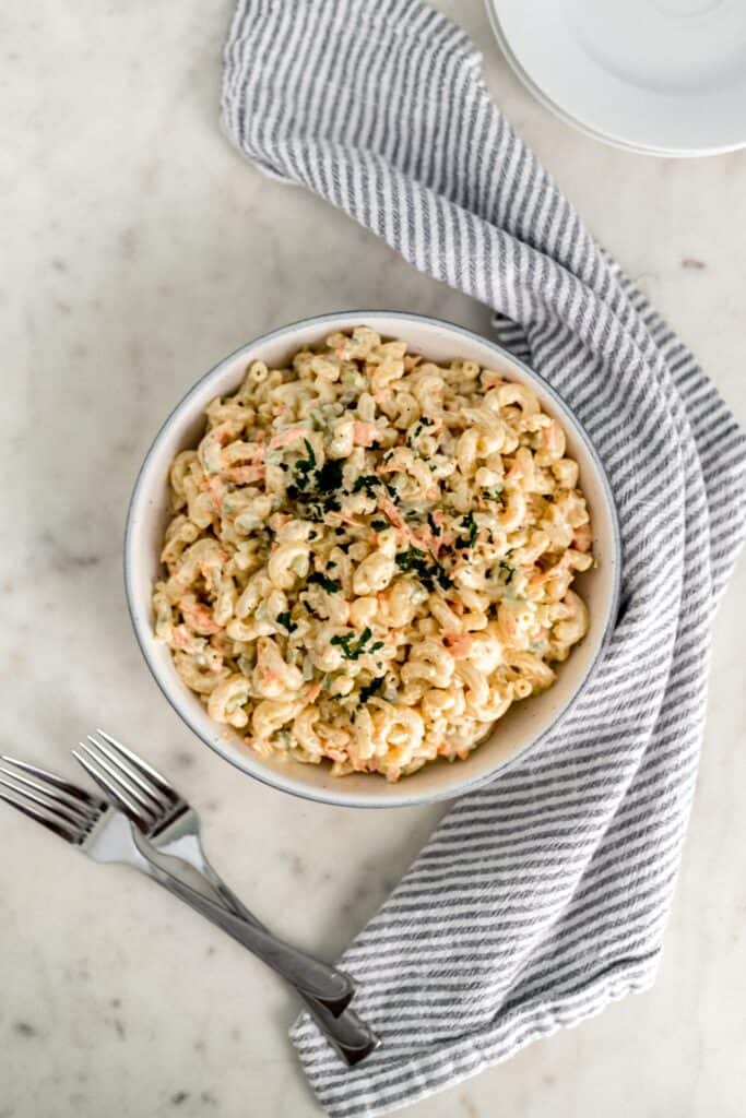overhead view macaroni salad in a large white bowl with forks, white plates, and cloth napkin 