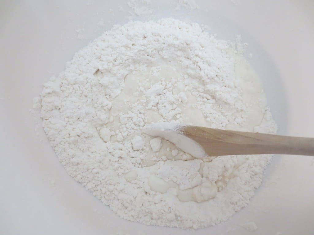 milk added to flour mixture in white mixing bowl with wooden spoon