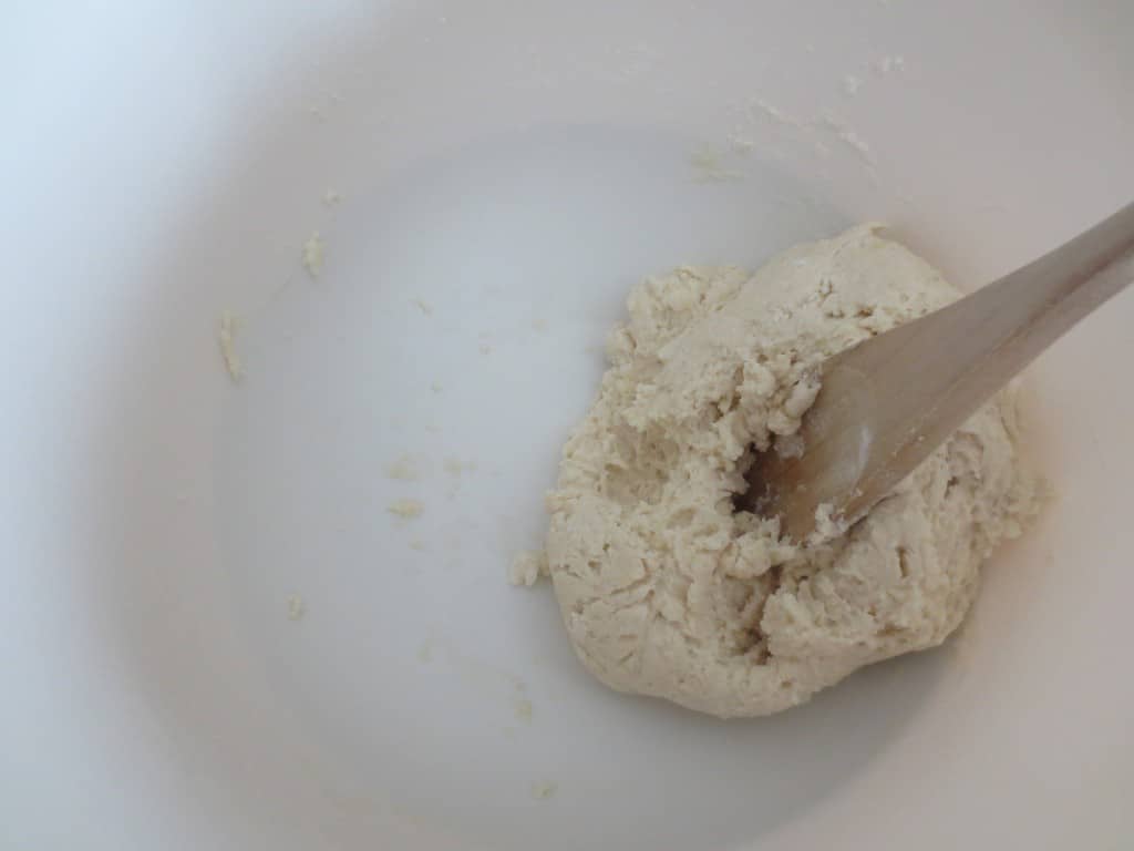 dough ball for biscuits in white mixing bowl with wooden spoon stirring