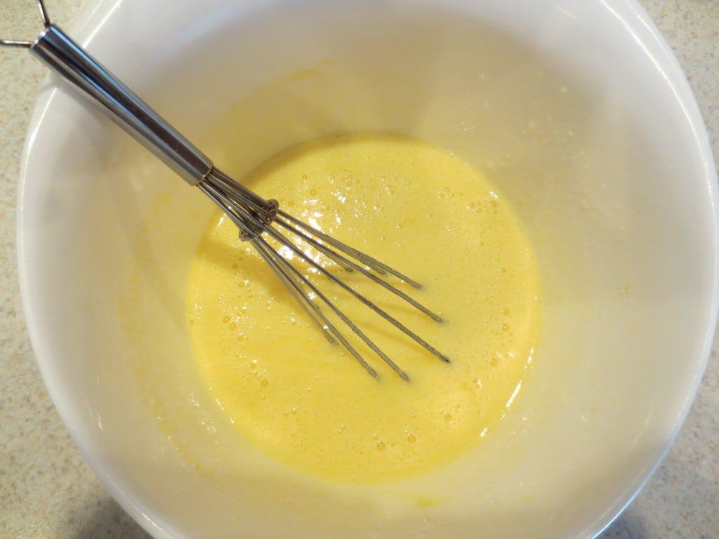 filling for lemon bars in white mixing bowl with whisk