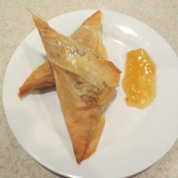 two finished samosas on a small white plate with sauce