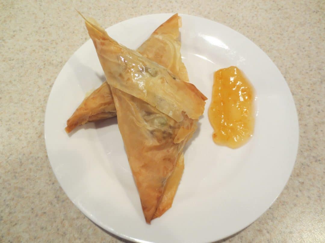 two finished samosas on a small white plate with sauce