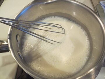 Custard base ingredients in saucepan with whisk.