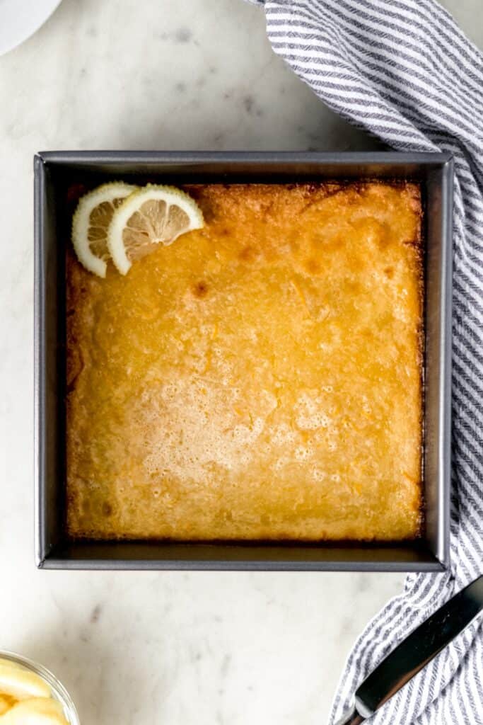 overhead view original lemon bars in a baking dish with napkin, knife, and lemon slices
