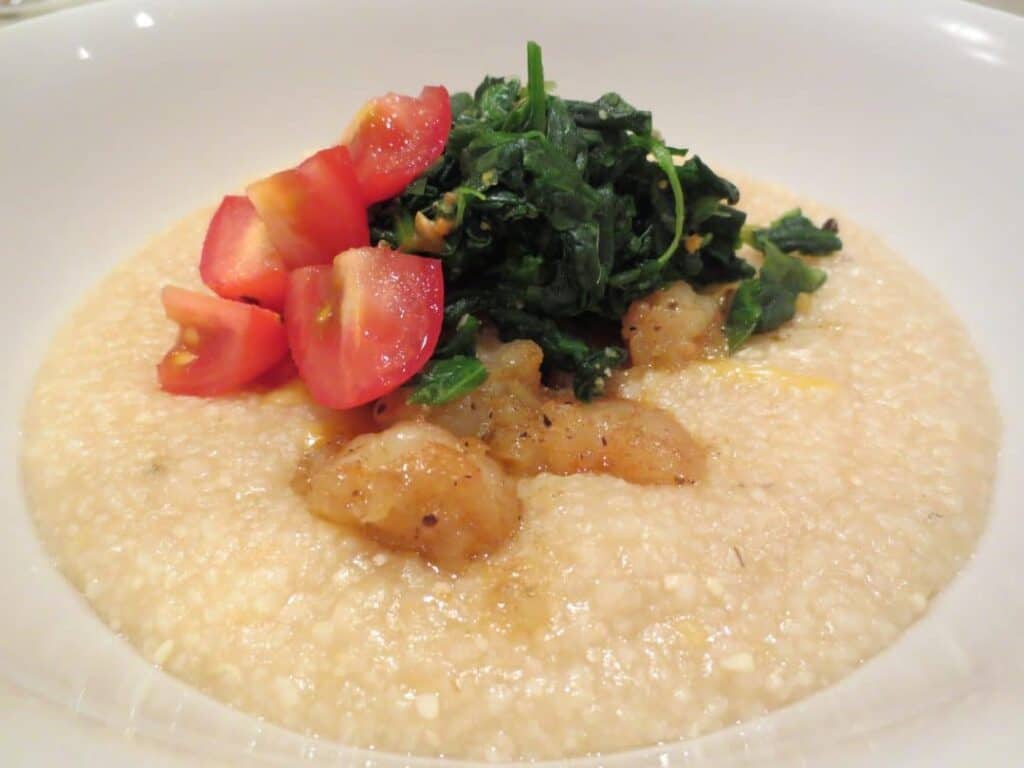 close up side view of white bowl with shrimp and grits in it topped with spinach and tomato 