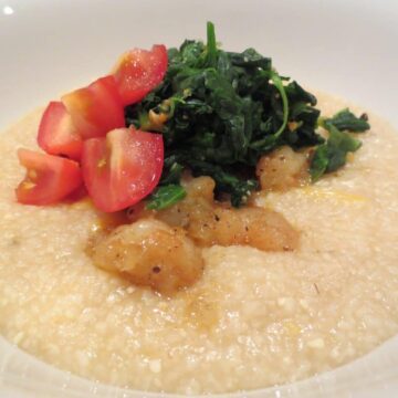 close up side view of white bowl with shrimp and grits in it topped with spinach and tomato