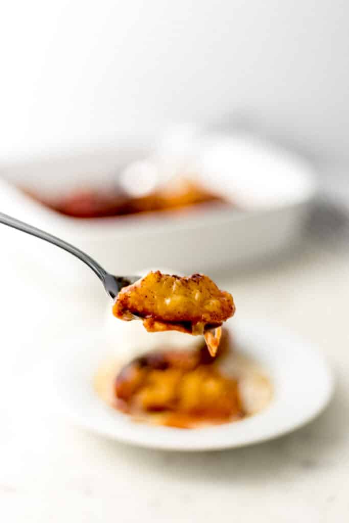Hand holding fork with baked peaches on it over white plate 