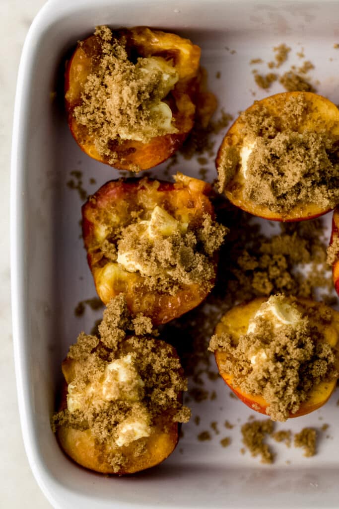 peaches in white baking dish cut in half topped with butter and brown sugar 