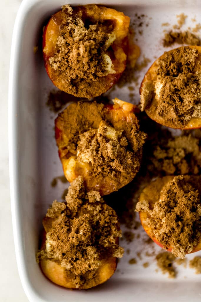 peaches cut in half in white baking dish topped with butter, brown sugar, and ground cinnamon 