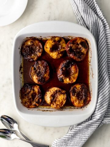 overhead view brown sugar baked peaches in white baking dish with white plates, spoons, cloth napkin