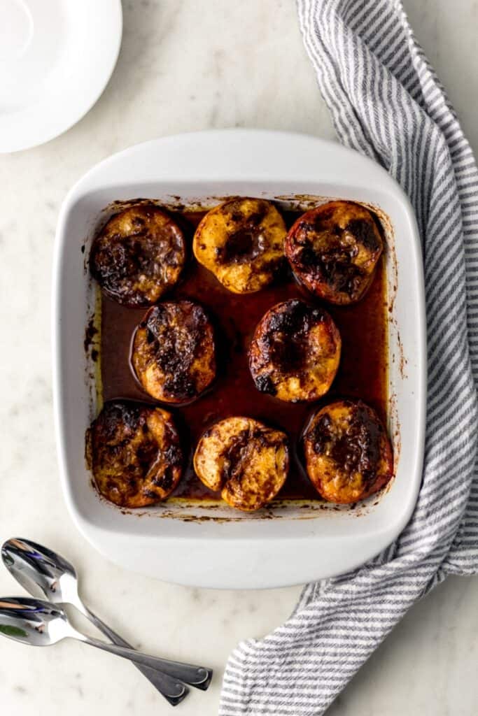 overhead view brown sugar baked peaches in white baking dish with white plates, spoons, cloth napkin 