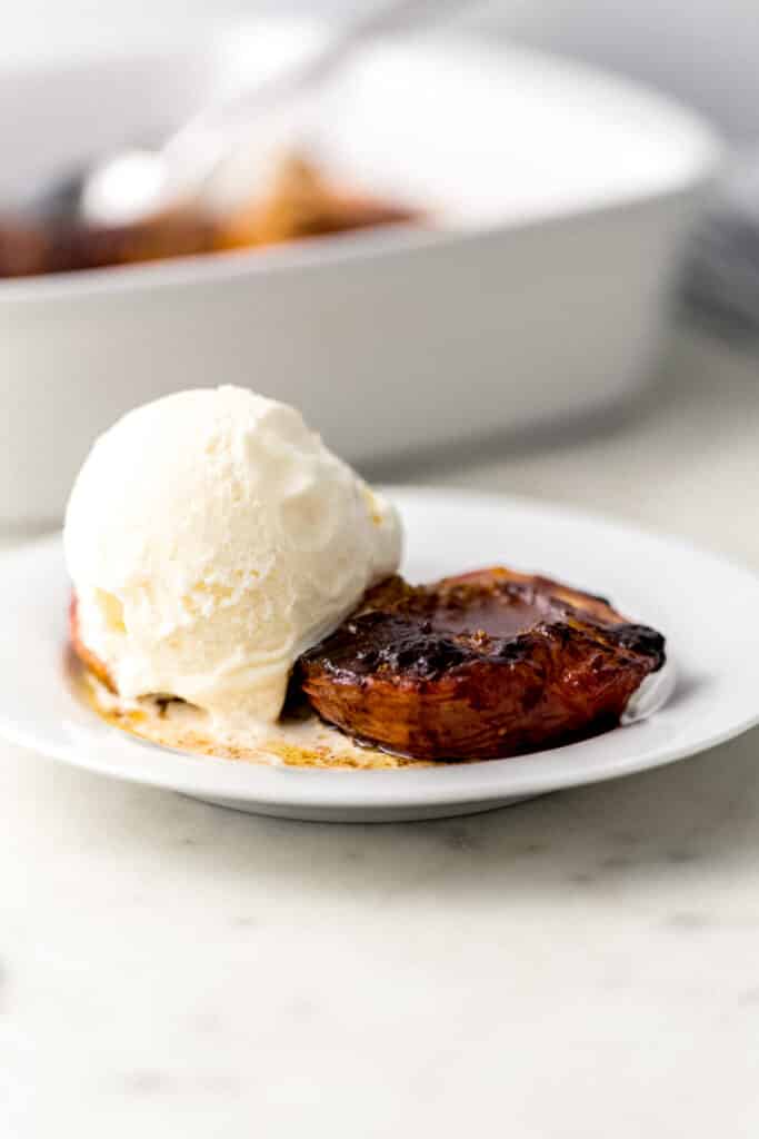 small white plate with 2 baked peaches on it with a scoop of vanilla ice cream 