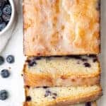 overhead view lemon blueberry bread cut into slices next to a small white bowl of fresh blueberries
