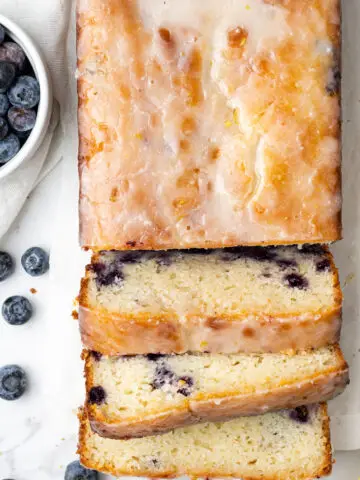 overhead view lemon blueberry bread cut into slices next to a small white bowl of fresh blueberries