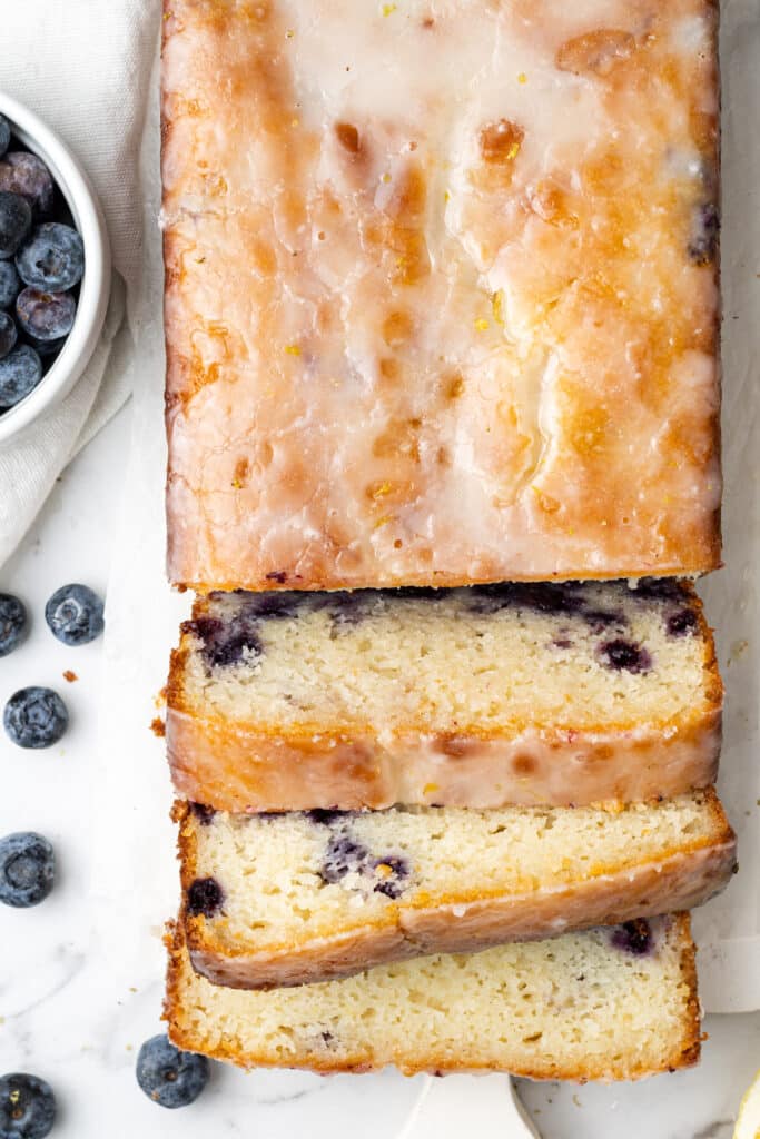 overhead view lemon blueberry bread cut into slices next to a small white bowl of fresh blueberries