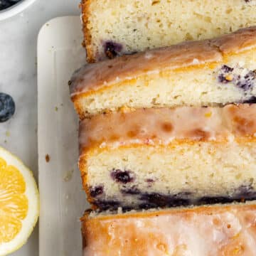 lemon blueberry bread on rectangle white platter beside a lemon and blueberries