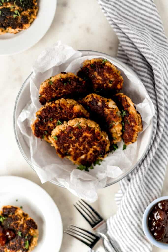 salmon patties in large white bowl with striped napkin and fork