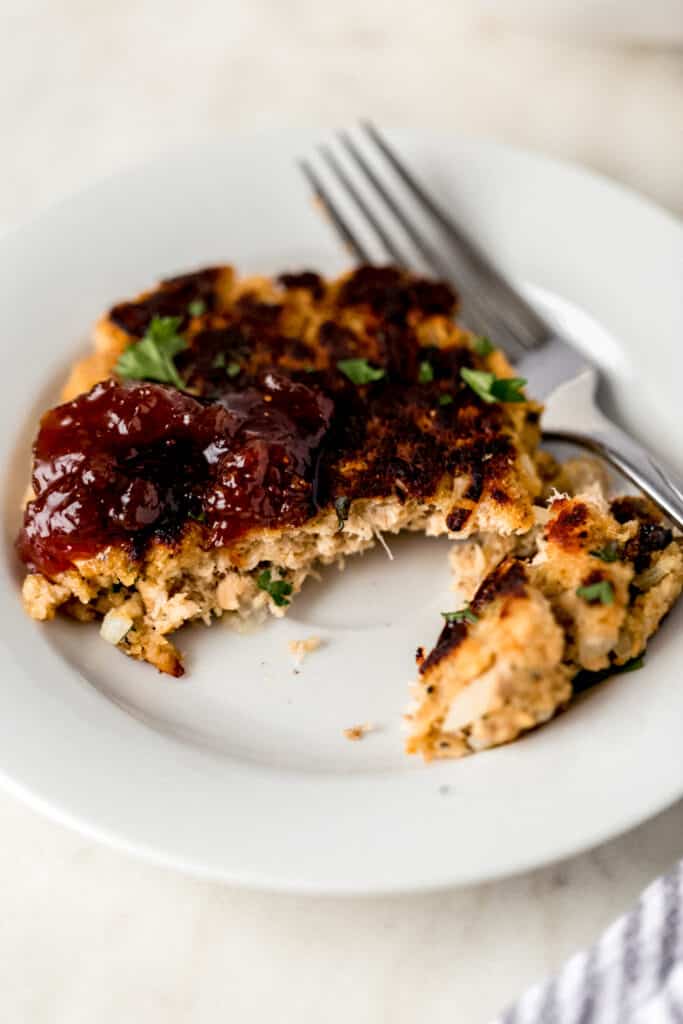 single salmon patty on white plate topped with preserves and a fork on the side 