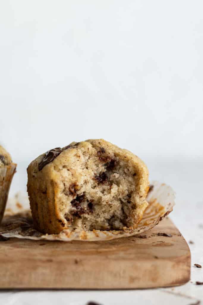 close up side view single muffin with a bite in it on a wooden surface. 