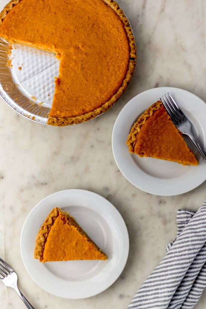 overhead view of cut sweet potato pie with two slice on two white plates.
