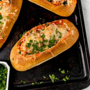 finished meatball subs on sheet pan next to small bowl of fresh parsley