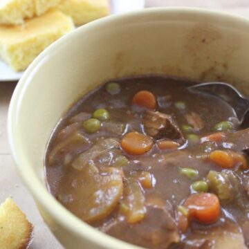 yellow bowl with finished beef stew in it with spoon and cornbread in the background