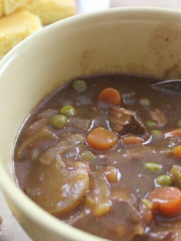 yellow bowl with finished beef stew in it with spoon and cornbread in the background