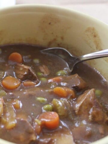 yellow bowl with finished beef stew in it with spoon and cornbread in the background
