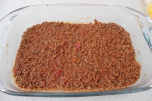 Meat sauce added to the bottom of a glass baking dish.