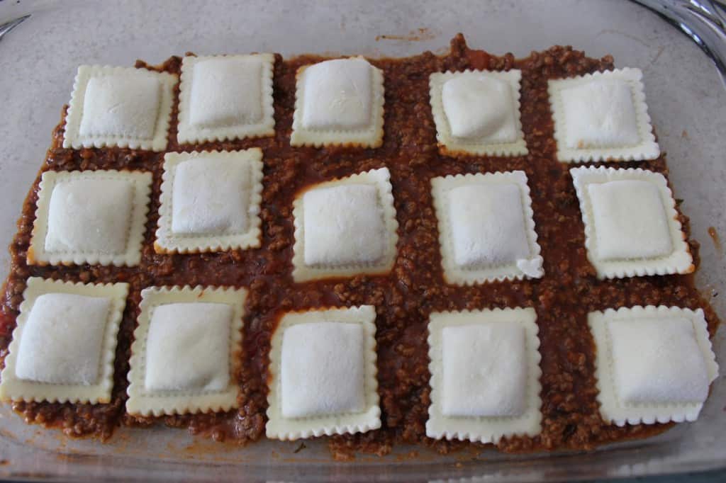 frozen cheese ravioli on top of meat sauce in glass baking dish