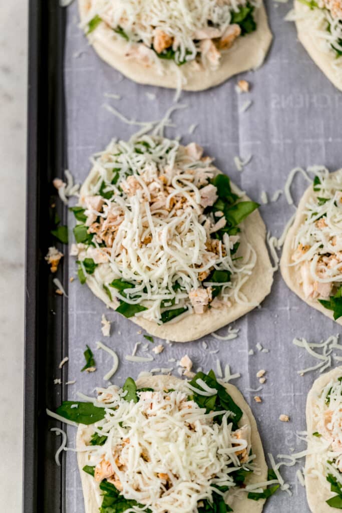 raw biscuits topped with ingredients to make mini chicken alfredo pizzas 
