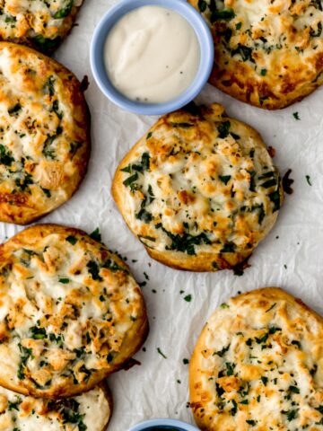 mini chicken alfredo biscuit pizzas on parchment with dipping sauce in small blue bowl