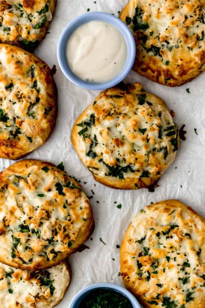 mini chicken alfredo biscuit pizzas on parchment with dipping sauce in small blue bowl 