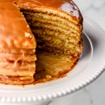 Close up side view of sliced cake on white platter on marble surface.