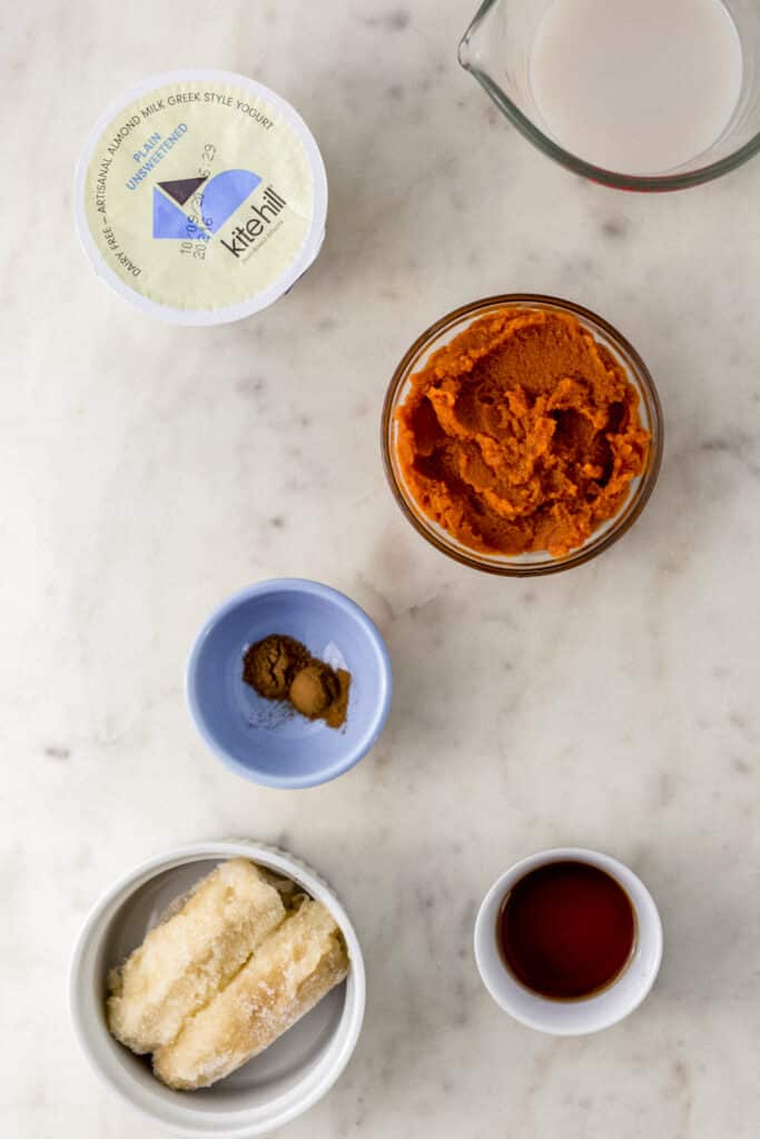 ingredients for pumpkin smoothie in small bowls on marble surface 