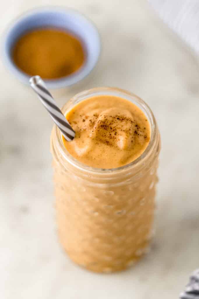 pumpkin spice smoothie in glass with straw and small bowl with pumpkin spice in background. 